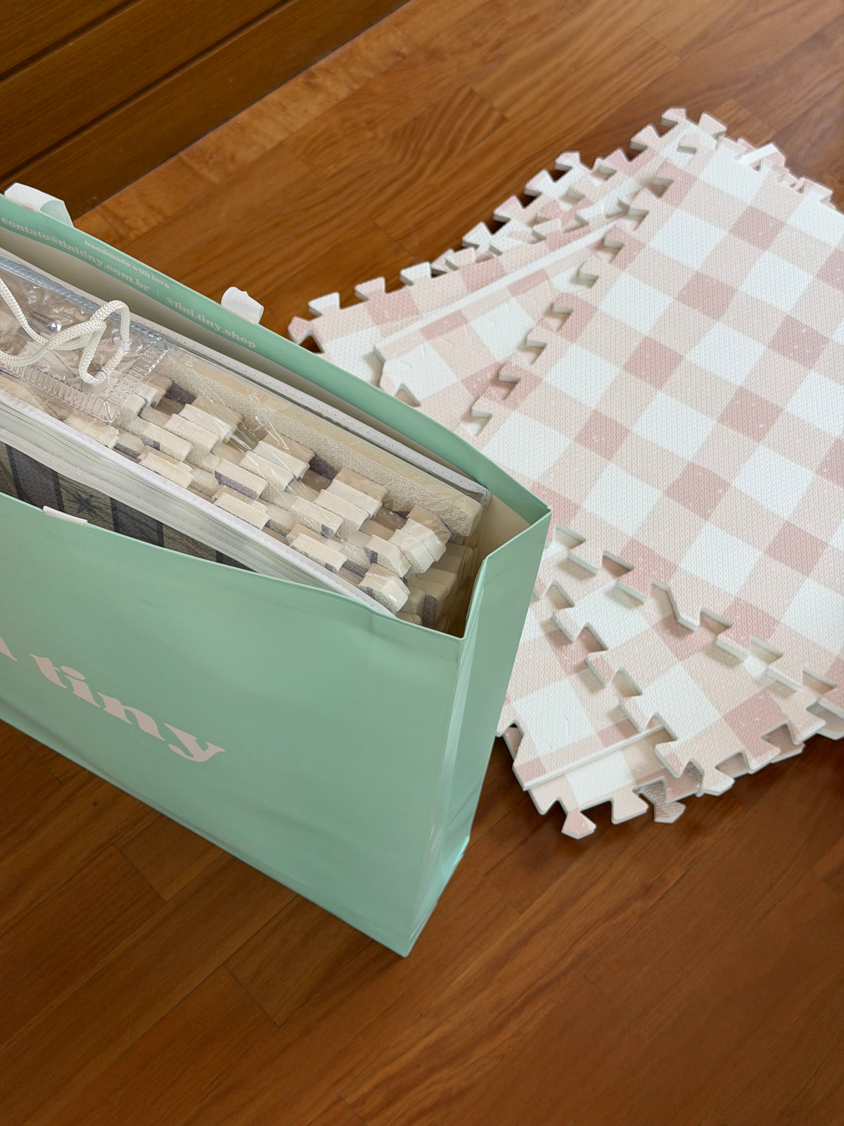 Placas soltas do tapetinho Vichy khaki ao lado da sacola de papel tini tiny verde-água, com um estojo de PVC dentro