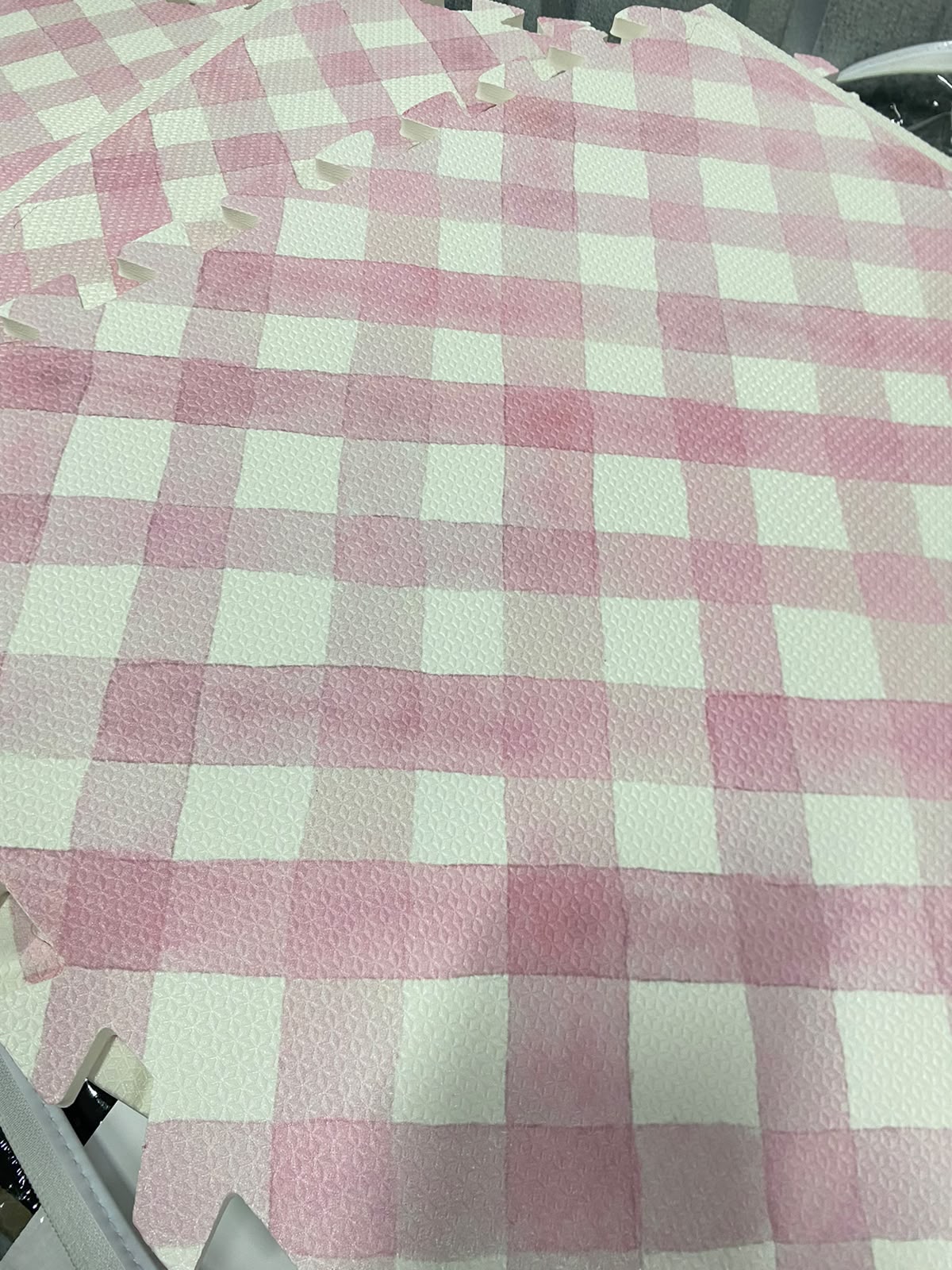 Close das placas do tapete infantil de EVA Criss Cross rosa montadas, com o xadrez aquarelado, a textura do EVA e os encaixes na borda