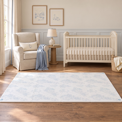 Tapete infantil de EVA Toile de Jouy Ducks azul montado no quarto de bebê, com berço branco, poltrona com almofada de patinho e manta azul, e quadros de casinha no lago e de pata na parede