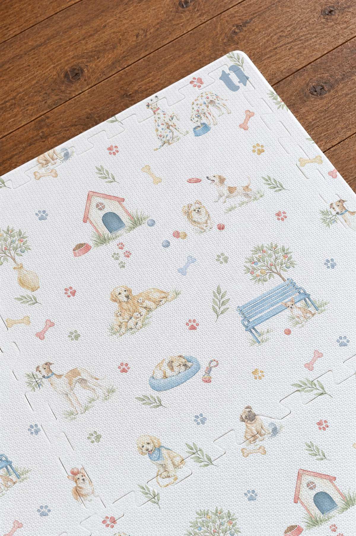 Close do canto do tapete infantil de EVA Toile de Jouy Dogs multicolorido montado sobre piso de madeira, com casinha vermelha, banco azul, caminha azul, cachorrinhos em aquarela e os encaixes das placas
