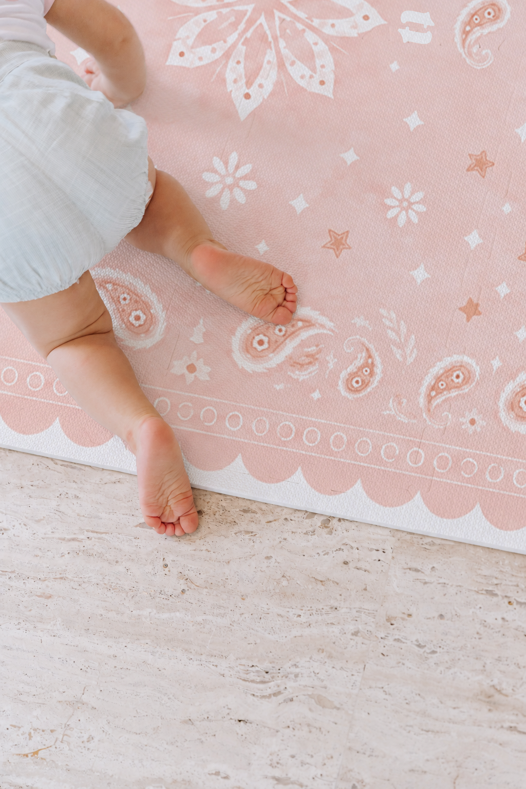 Bebê de roupinha clara de bruços no tapete infantil de EVA Bandana rosa, com paisleys, florzinhas e a borda ondulada, sobre piso de pedra clara