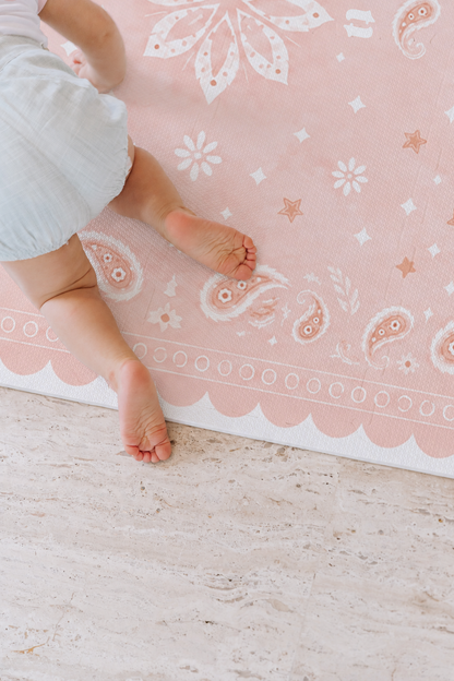 Bebê de roupinha clara de bruços no tapete infantil de EVA Bandana rosa, com paisleys, florzinhas e a borda ondulada, sobre piso de pedra clara