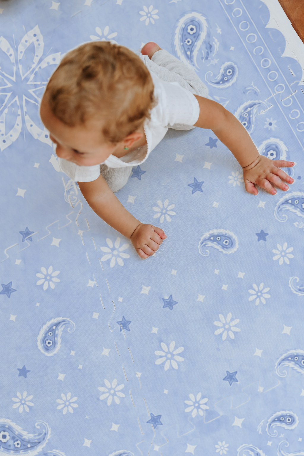 Bebê de roupa branca engatinhando no tapete infantil de EVA Bandana azul, com paisleys, florzinhas e estrelinhas, visto de cima