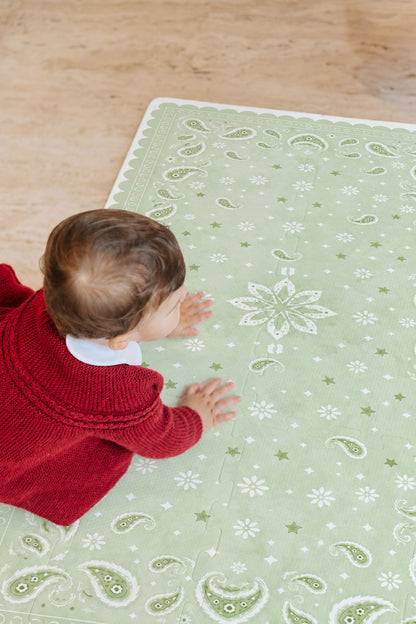 Bebê de casaquinho vermelho engatinhando sobre o tapete infantil de EVA Bandana verde, visto de cima