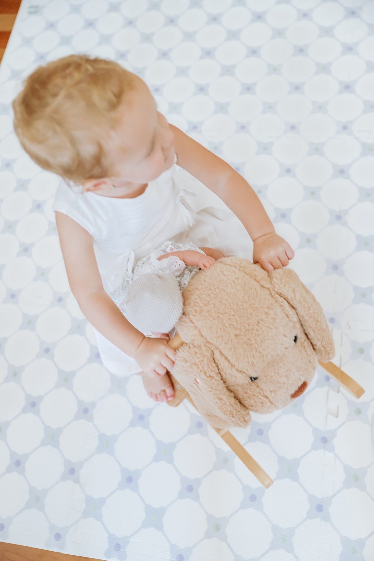Criança sentada num cachorrinho de pelúcia de balanço sobre o tapete infantil de EVA Flower Power azul