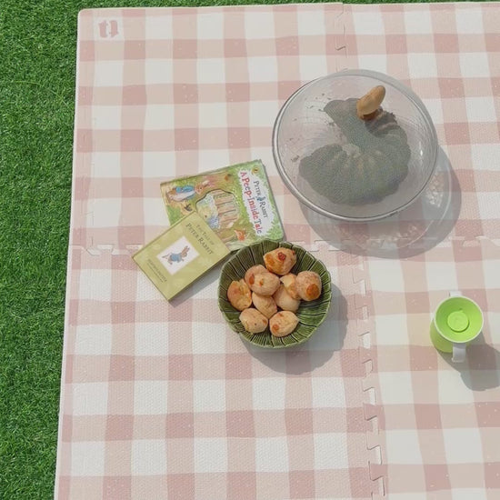 Vídeo do tapete infantil de EVA Vichy khaki montado sobre a grama, com livrinhos, tigela de pães de queijo e copo de criança, como num piquenique