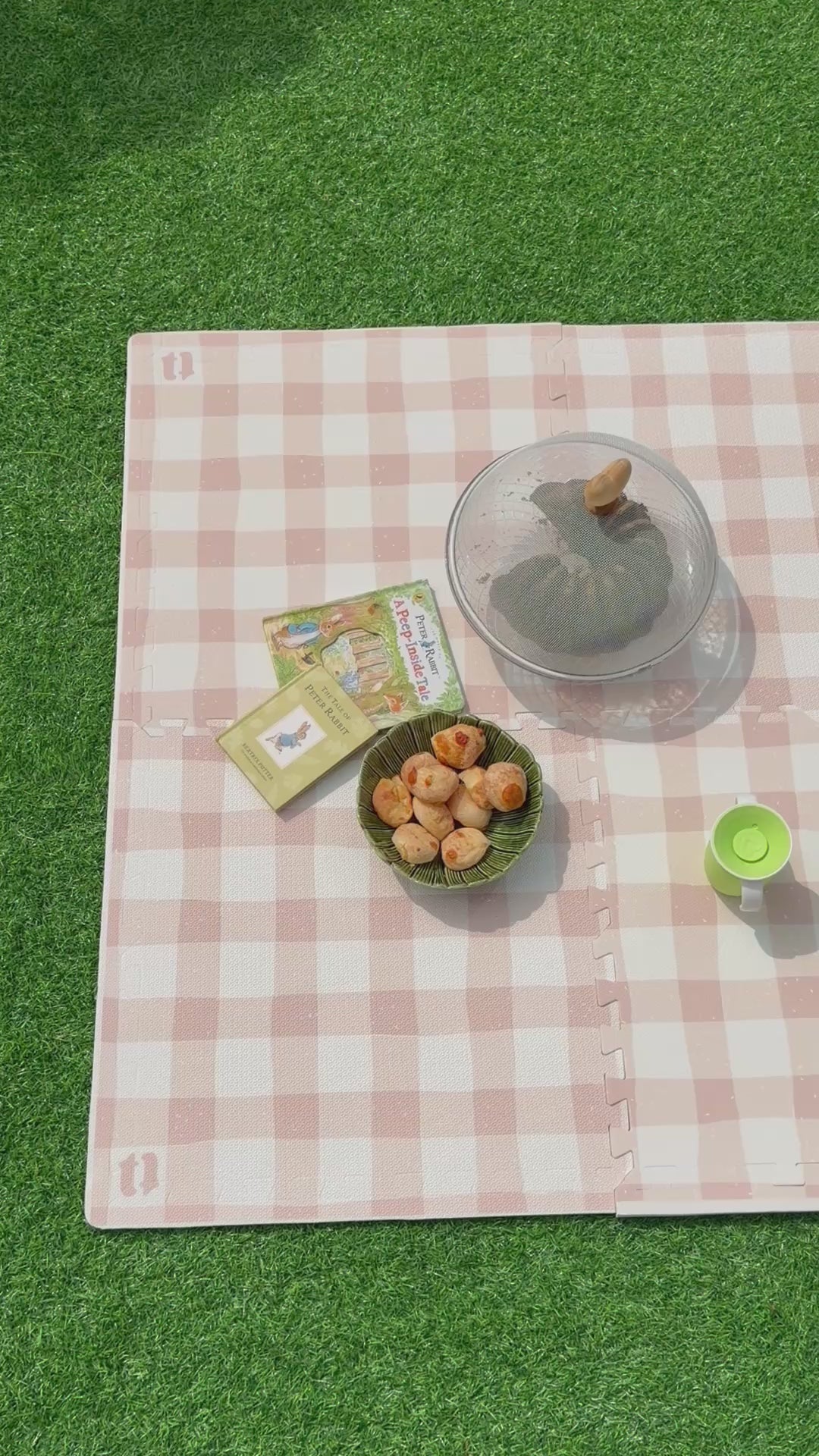 Vídeo do tapete infantil de EVA Vichy khaki montado sobre a grama, com livrinhos, tigela de pães de queijo e copo de criança, como num piquenique