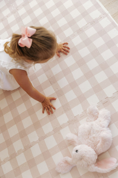 Criança de laço rosa no cabelo engatinhando no tapete infantil de EVA Vichy khaki, com um coelhinho de pelúcia ao lado